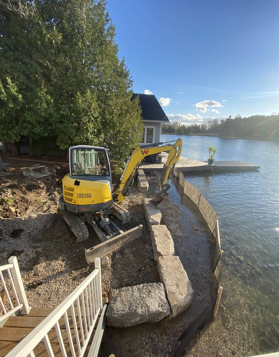 Mini excavator placing armour stone blocks for a lakeside retaining wall