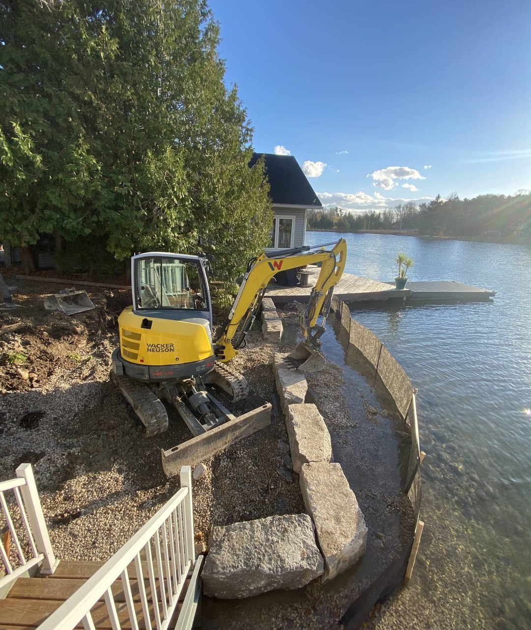 Mini excavator placing armour stone blocks for a lakeside retaining wall