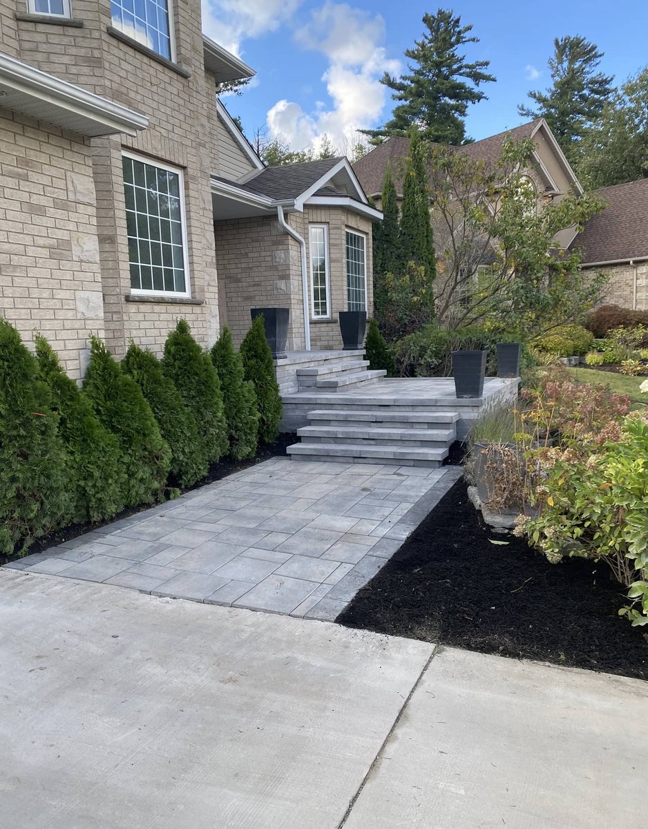Paver walkway with stone steps leading to the front entrance of a large stone home