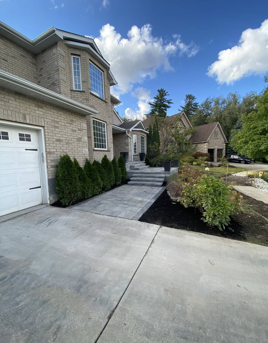 Wide stamped concrete walkway with steps and landscaped border alongside a brick home