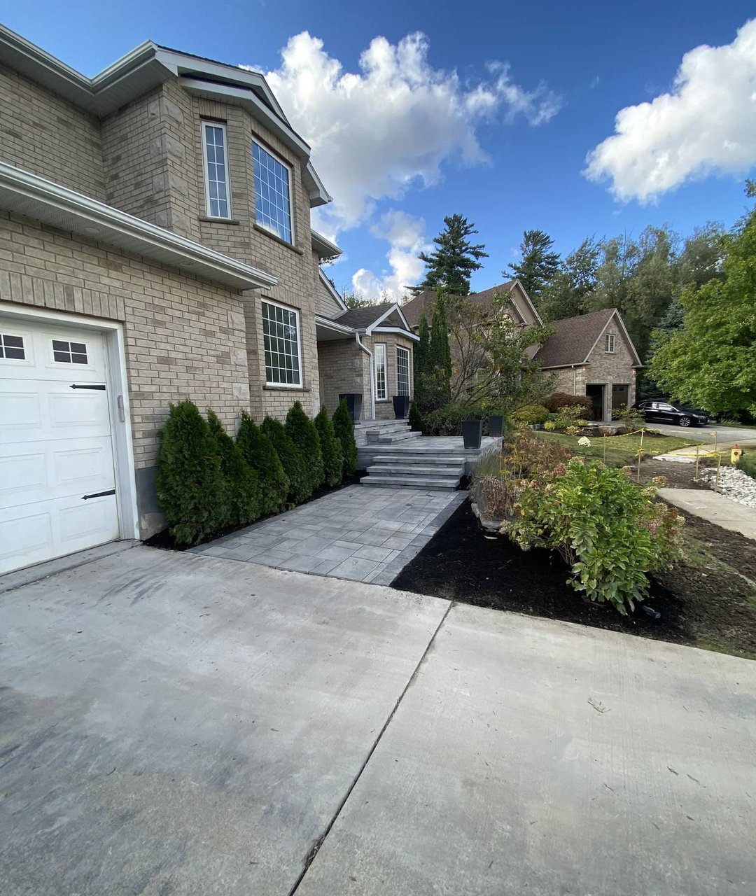 Wide stamped concrete walkway with steps and landscaped border alongside a brick home