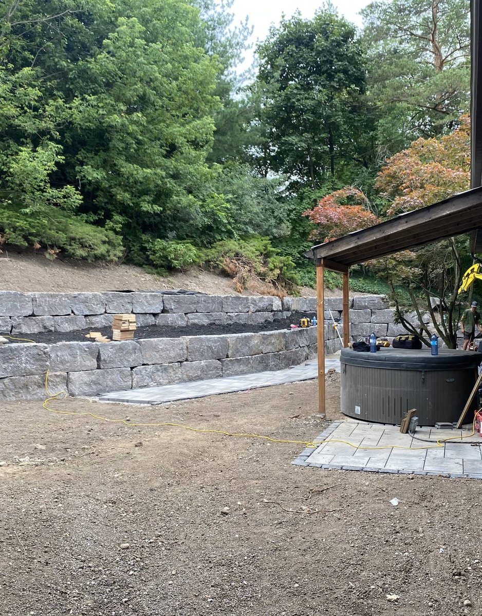 Tiered armour stone retaining wall built into a backyard slope with hot tub on a paver pad
