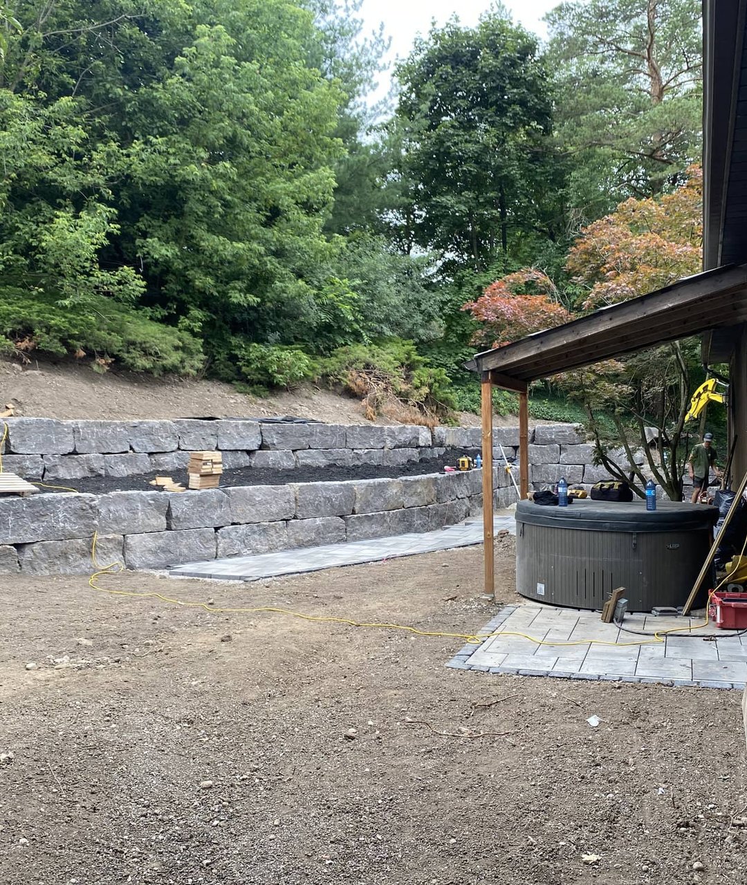 Tiered armour stone retaining wall built into a backyard slope with hot tub on a paver pad