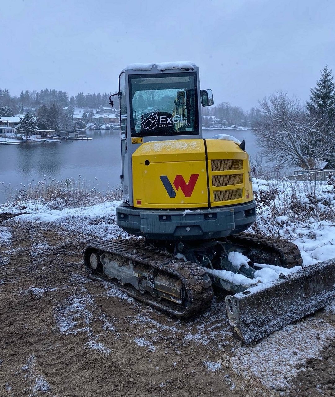 ExCL-branded compact tracked excavator parked on a snowy lakeside lot