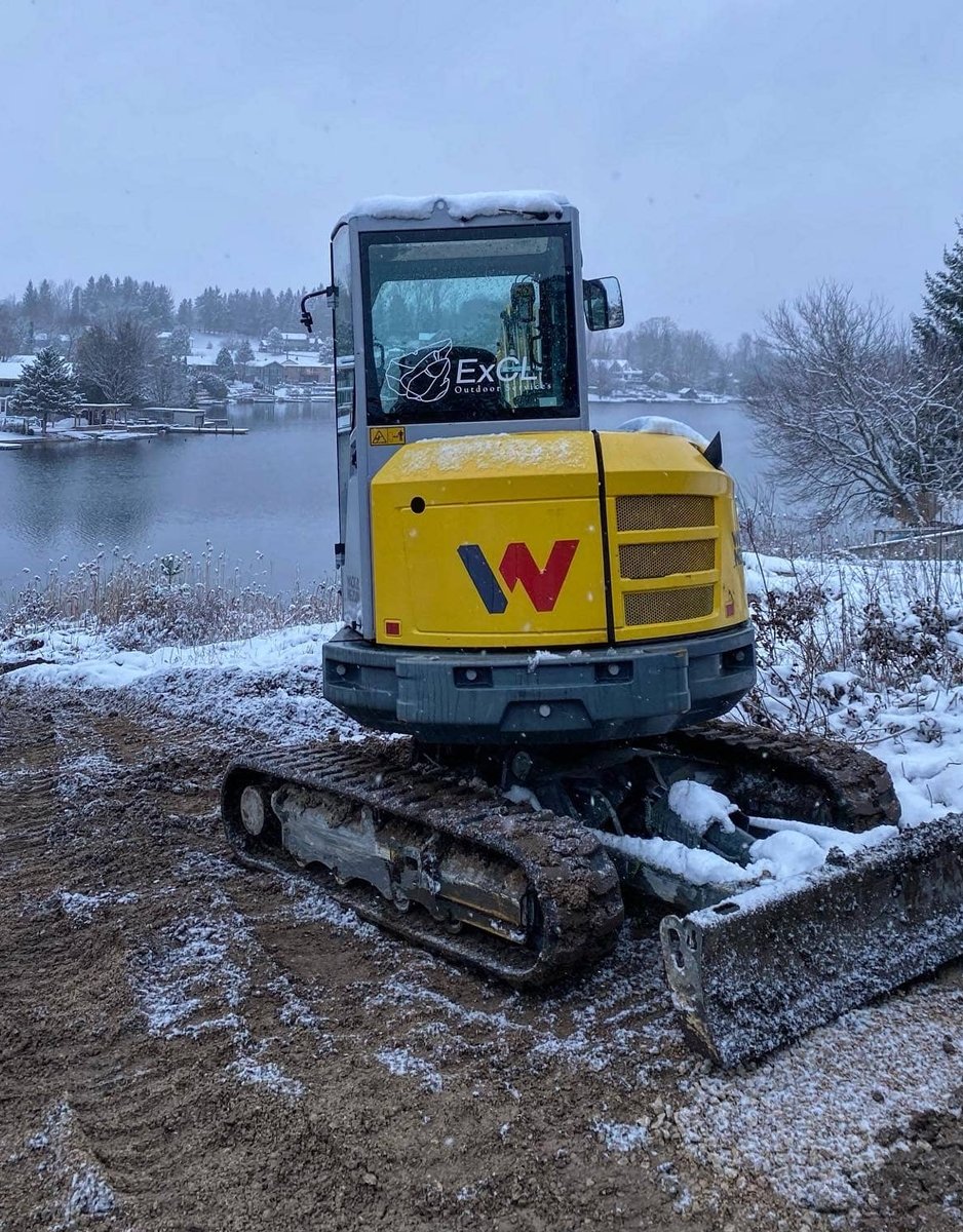 ExCL-branded compact tracked excavator parked on a snowy lakeside lot