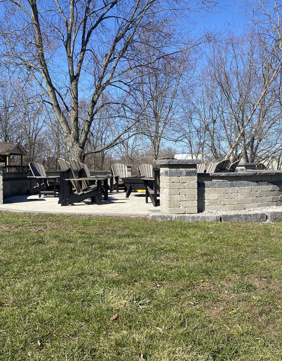 Curved stone seating wall surrounding a poured concrete fire pit pad in a backyard