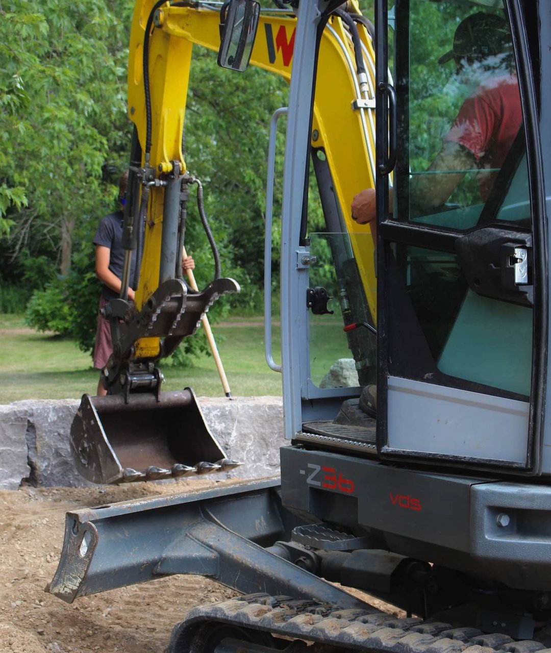 ExCL operator using a mini excavator to set armour stone blocks on site