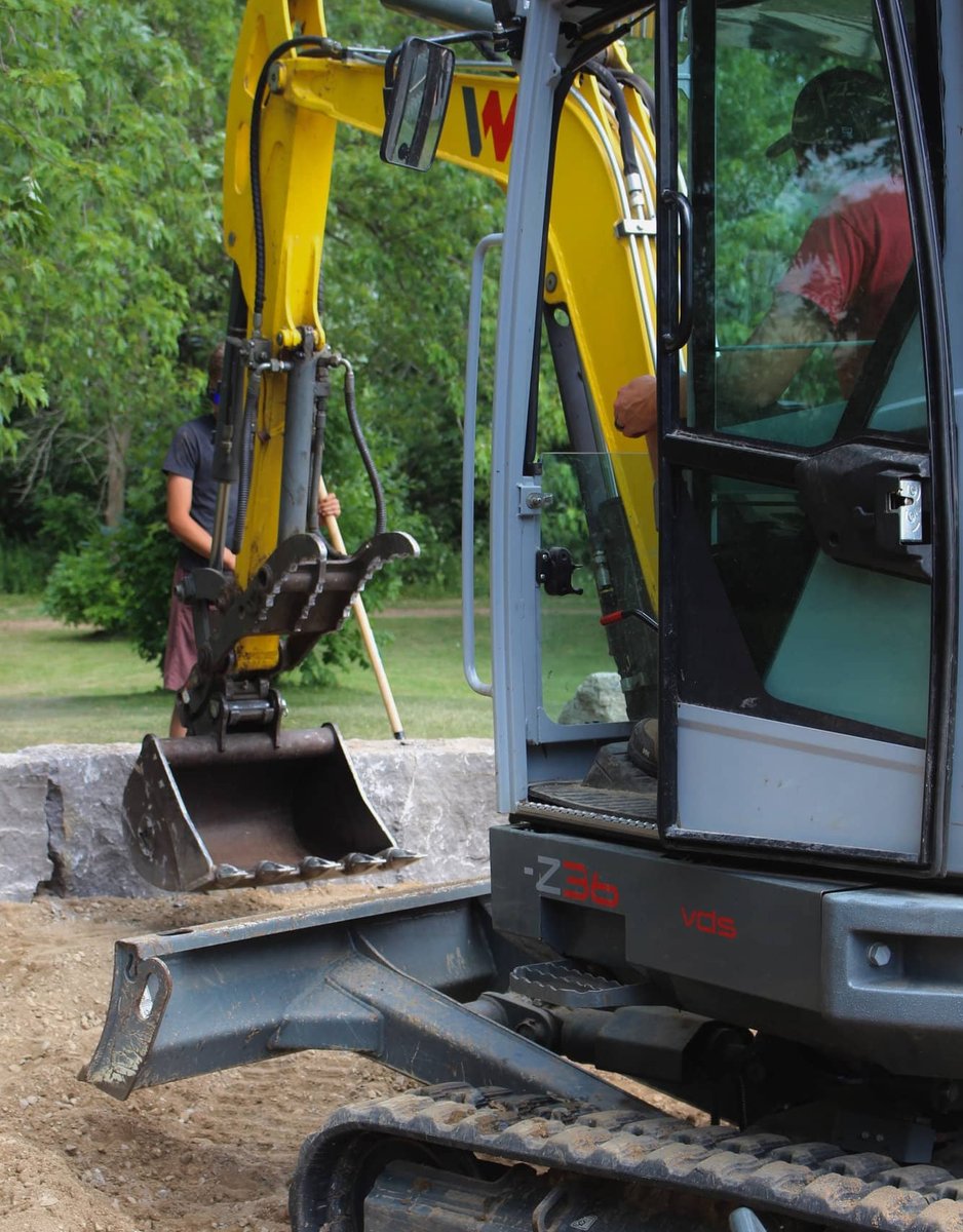 ExCL operator using a mini excavator to set armour stone blocks on site