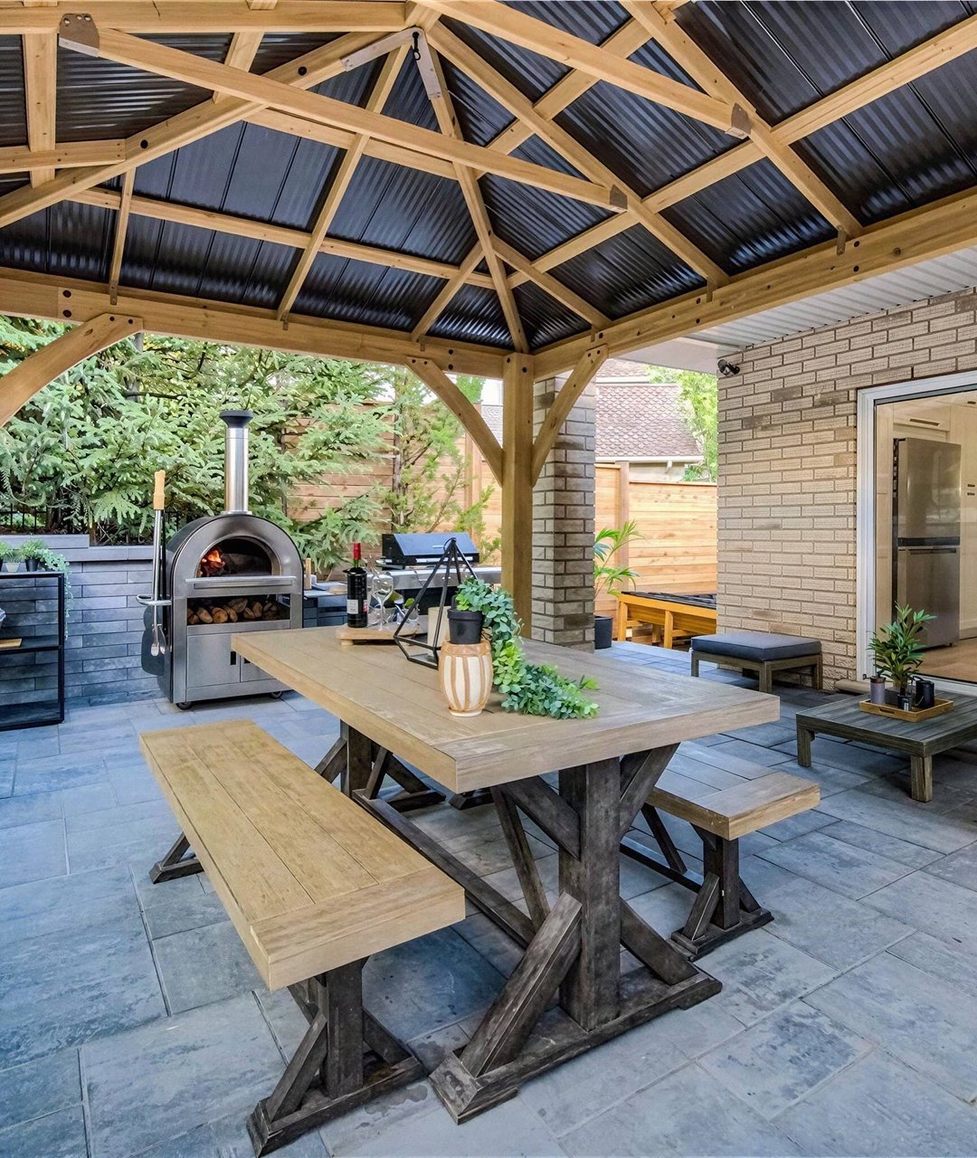 Covered outdoor pavilion with pizza oven, dining table and natural stone patio