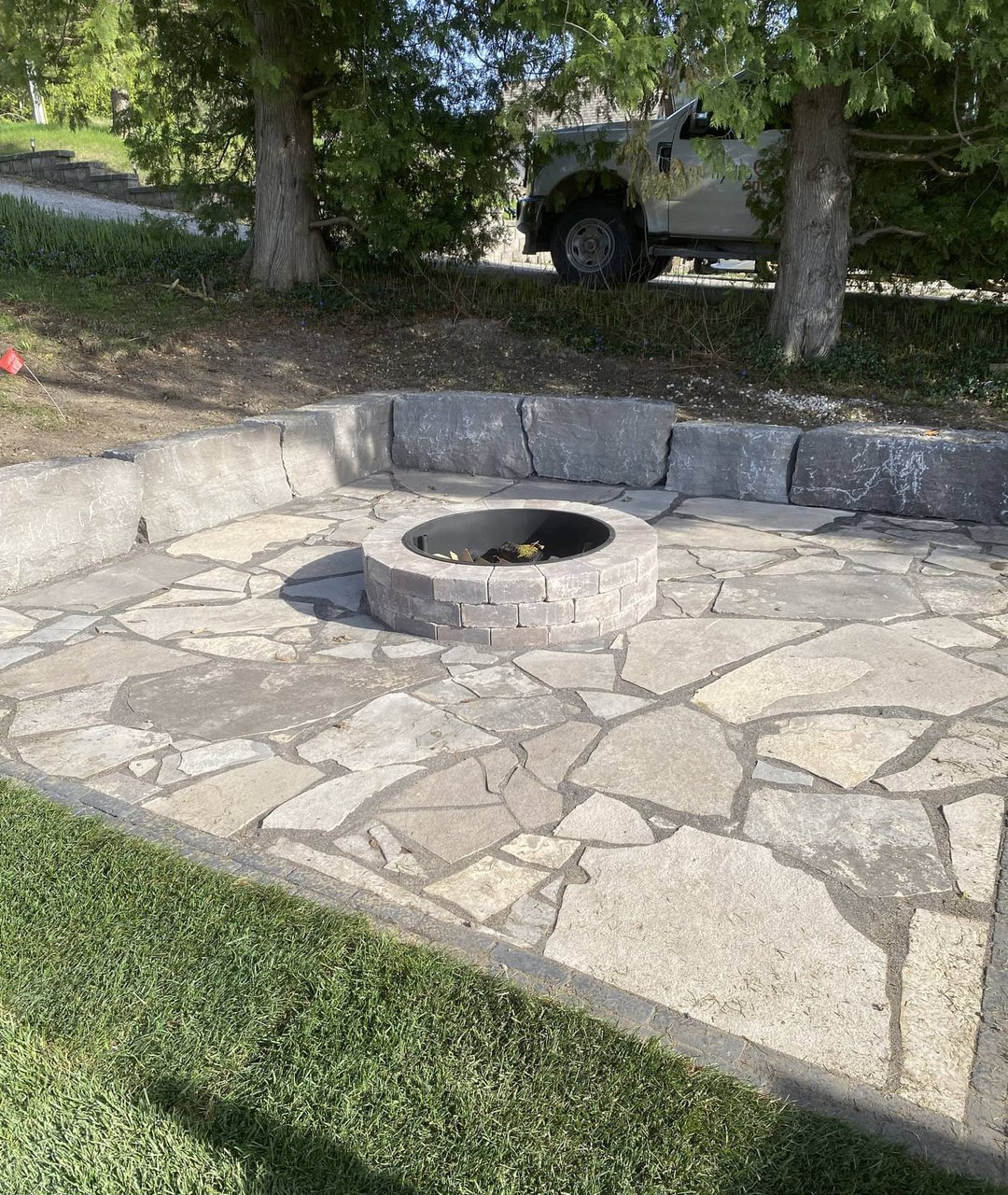 Round stone fire pit set in a flagstone patio with a curved stacked-stone seating wall