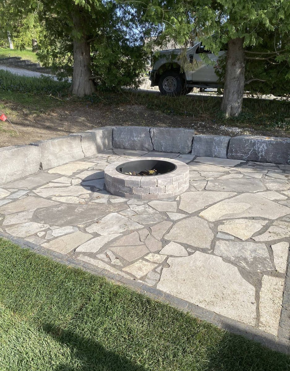 Round stone fire pit set in a flagstone patio with a curved stacked-stone seating wall