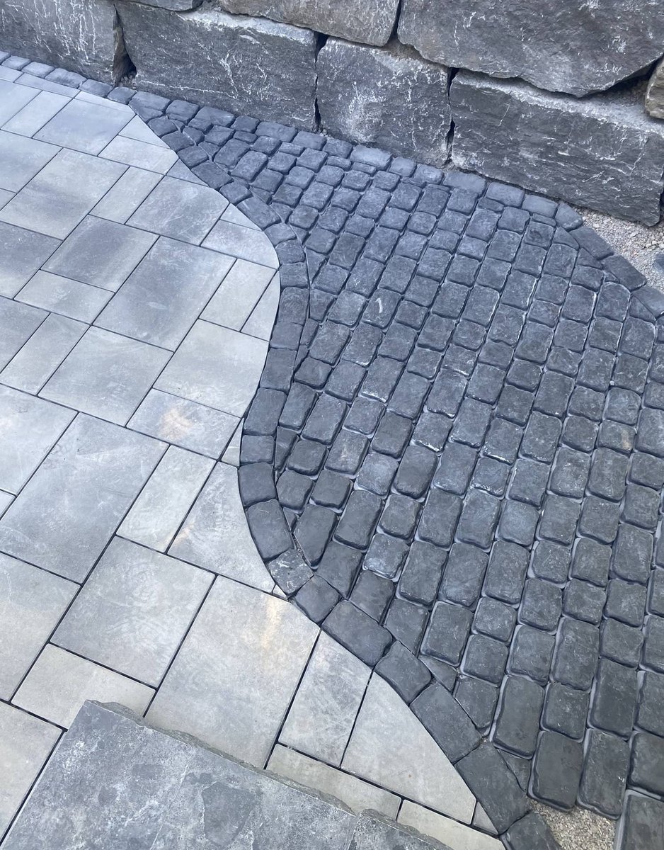 Detailed paver patio with curved cobblestone inlay against a stacked stone wall
