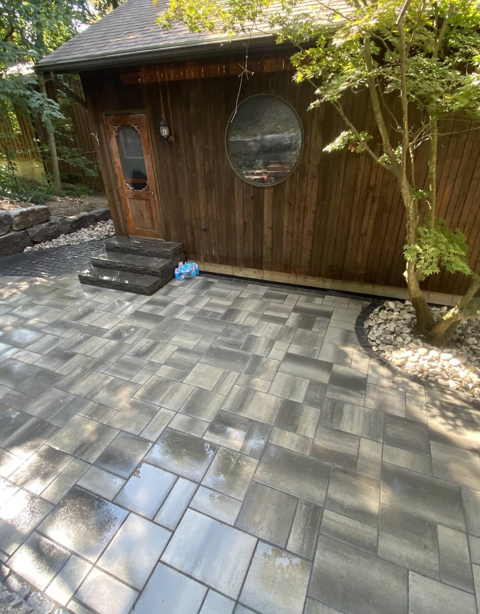Freshly washed grey paver patio in front of a cedar-clad cabin with river rock border