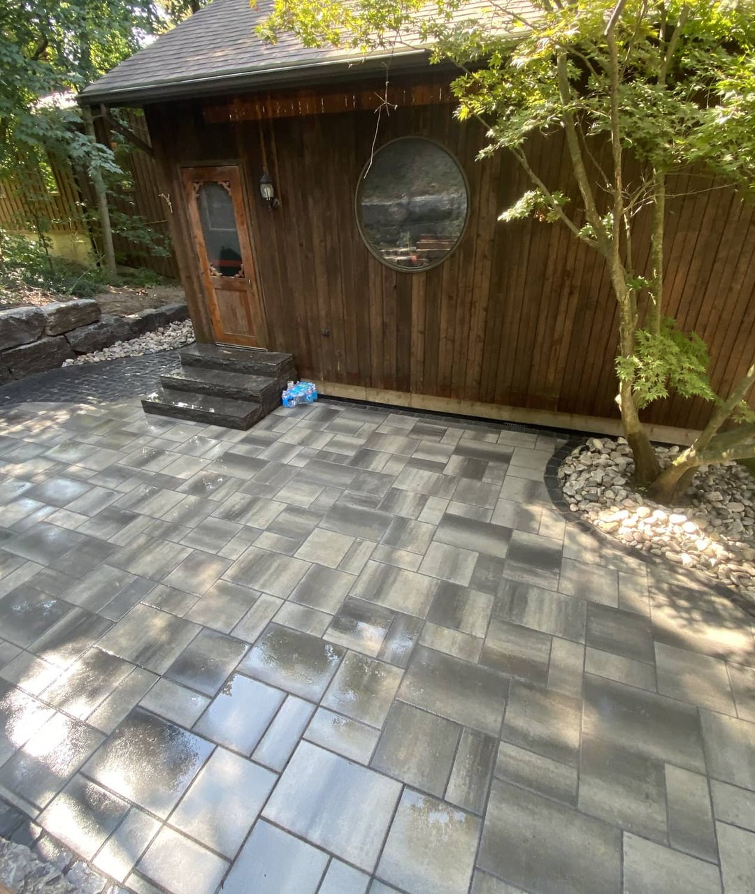 Freshly washed grey paver patio in front of a cedar-clad cabin with river rock border