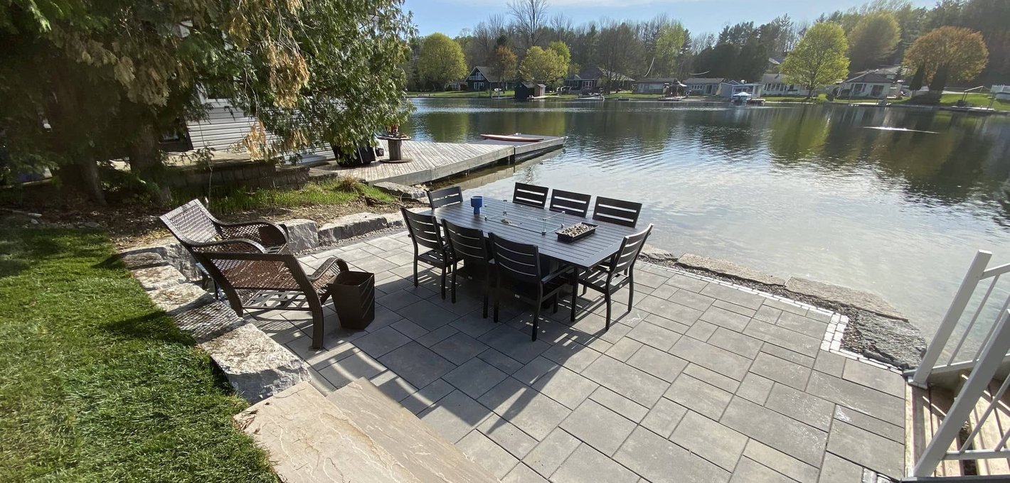 Stone hardscape patio with planted border alongside a finished home